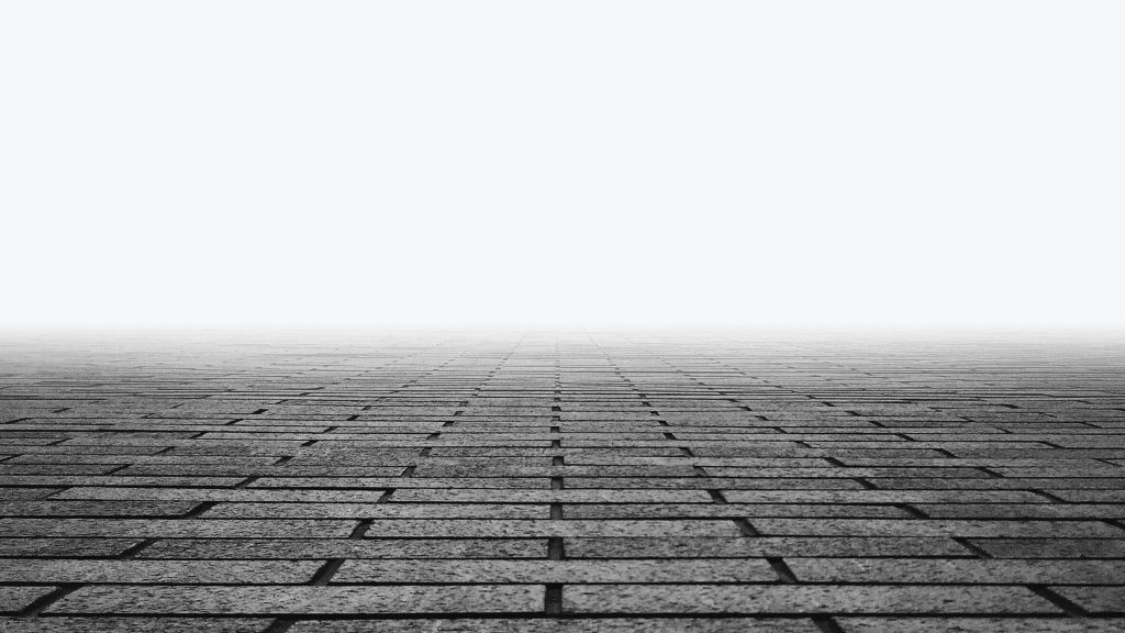 A perspective view of a brick pavement extending towards the horizon, meeting a bright, foggy sky. The bricks are uniformly laid out in a grid pattern, creating a sense of depth and infinity as they disappear into the distance.
