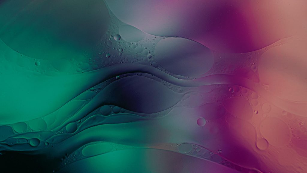 An abstract image featuring a blend of vibrant colors, including shades of green, purple, and pink, with fluid, wavy patterns and varying bubble-like textures throughout the composition. The overall effect is dreamy and ethereal.